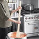 A person holding a Choice wood paddle over a large pot of soup.