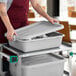 A woman putting a gray Choice polypropylene container with a lid into a cart.