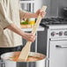 A person using a Choice 30" Wood Paddle to stir a pot of soup on a stove.