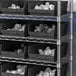 A metal shelf with black Regency plastic bins on it.