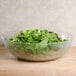 A Cambro pebbled serving bowl filled with green leaves on a table.