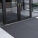 A gray unbacked scraper mat roll in front of glass doors.