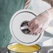 A person in gloves holding a Choice stainless steel bain marie cover over a bowl of food.