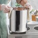 A person wearing gloves and holding a Choice stainless steel Bain Marie pot.