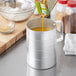 A person pouring liquid into a Choice aluminum measuring cup on a counter.