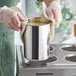 A person in gloves holding a stainless steel Bain Marie pot of liquid.