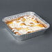 An 8" square foil cake pan with a white frosted cake inside.