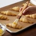 A person using a 1" boar bristle pastry brush to baste croissants.