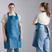 Two women wearing navy blue adjustable vinyl aprons.