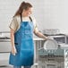 A woman wearing a navy blue Choice vinyl apron and gloves putting a plate in a dishwasher.