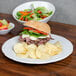 A Tuxton Chicago bright white china plate with a sandwich, chips, and salad.