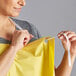 A woman holding a yellow Choice lightweight vinyl apron with white ties.