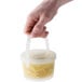 A hand using a clear plastic lid with a handle to hold a plastic soup container.