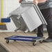 A man using a Lavex plastic dolly to move a large metal container.