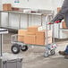 A Lavex hand truck with boxes on it being pushed by a man.