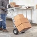 A man using a Lavex convertible hand truck to move a stack of cardboard boxes.