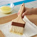 A hand holding a wood-handled boar bristle pastry brush over a white surface.