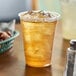 A clear Dart Polypropylene cup filled with ice and iced tea on a table.