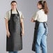 Two women wearing Choice black vinyl aprons and jeans on a counter in a professional kitchen.