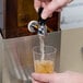 A hand filling a glass with liquid from a Cal-Mil stainless steel beverage dispenser.