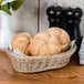 A honey oval plastic basket filled with rolls on a table.