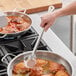 A person stirring food in a pan on a stove with a Choice stainless steel basting spoon.