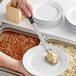 A person using a Choice stainless steel basting spoon with a black handle to serve food on a plate.