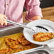 A person using a Choice stainless steel slotted spoon to serve food with sauce.