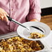 A woman using a Choice slotted basting spoon to serve food onto a plate.