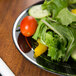 A Fineline Silver Splendor black plastic plate with silver bands filled with salad on a wood table.