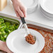 A hand using a Choice perforated basting spoon to serve beans onto a plate.