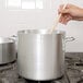 A hand holding a wooden spoon in a large silver Vollrath stock pot.