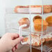 A hand holding a white plastic handle to a Cal-Mil three tier display case with pastries.