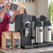 A woman holding a bag of coffee standing behind a Bunn Black Bulk Coffee Grinder.