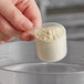 A hand holding a 25 cc polypropylene scoop full of powder over a container.