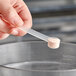 A hand holding a 1.25 cc polypropylene scoop filled with white powder.