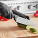 A person wearing black gloves uses a Schraf Santoku knife to cut a cucumber.