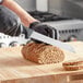 A person using a Schraf serrated bread knife to cut a loaf of bread on a cutting board.