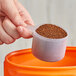 A hand using a 94 cc Polypropylene Scoop to pour brown powder into a container.