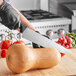 A person using a Schraf serrated chef knife to cut a squash.