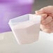 A hand holding a white 8 oz. polypropylene measuring cup filled with a white substance.