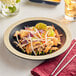 An Acopa matte black melamine plate with a medium ivory rim holding chicken salad with chopsticks on it.