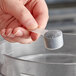 A hand holding a 5 cc polypropylene scoop with a grey powder.