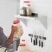 A woman in a professional kitchen placing a plastic container of brown grains on a Regency stainless steel wall shelf.