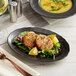 An Acopa Armor Gray scalloped porcelain platter with a bowl of soup and a salad on a table.