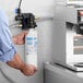 A man holding a Bunn single water filtration system in front of a coffee machine.