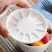 A hand holding a white Dart foam container with fruit inside.