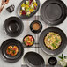 A table with Acopa Condesa matte gray dinnerware, including a bowl of fruit salad.