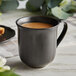 An Acopa Condesa armor gray porcelain mug filled with coffee on a table.
