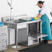 A stainless steel undercounter dishtable with a left-side sink, shown in use in a commercial kitchen setting.